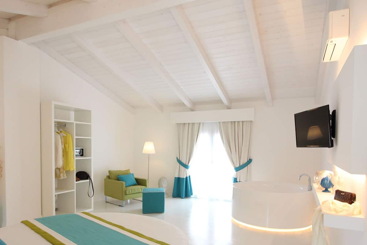 A modern bedroom with a large bed, a built-in wardrobe, a TV mounted on the wall, and a bathroom with a bathtub.