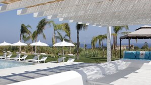 A poolside area with white lounge chairs and umbrellas, a covered seating area, and a view of the ocean. - Il Borghetto Resort & Spa (Tropea)
