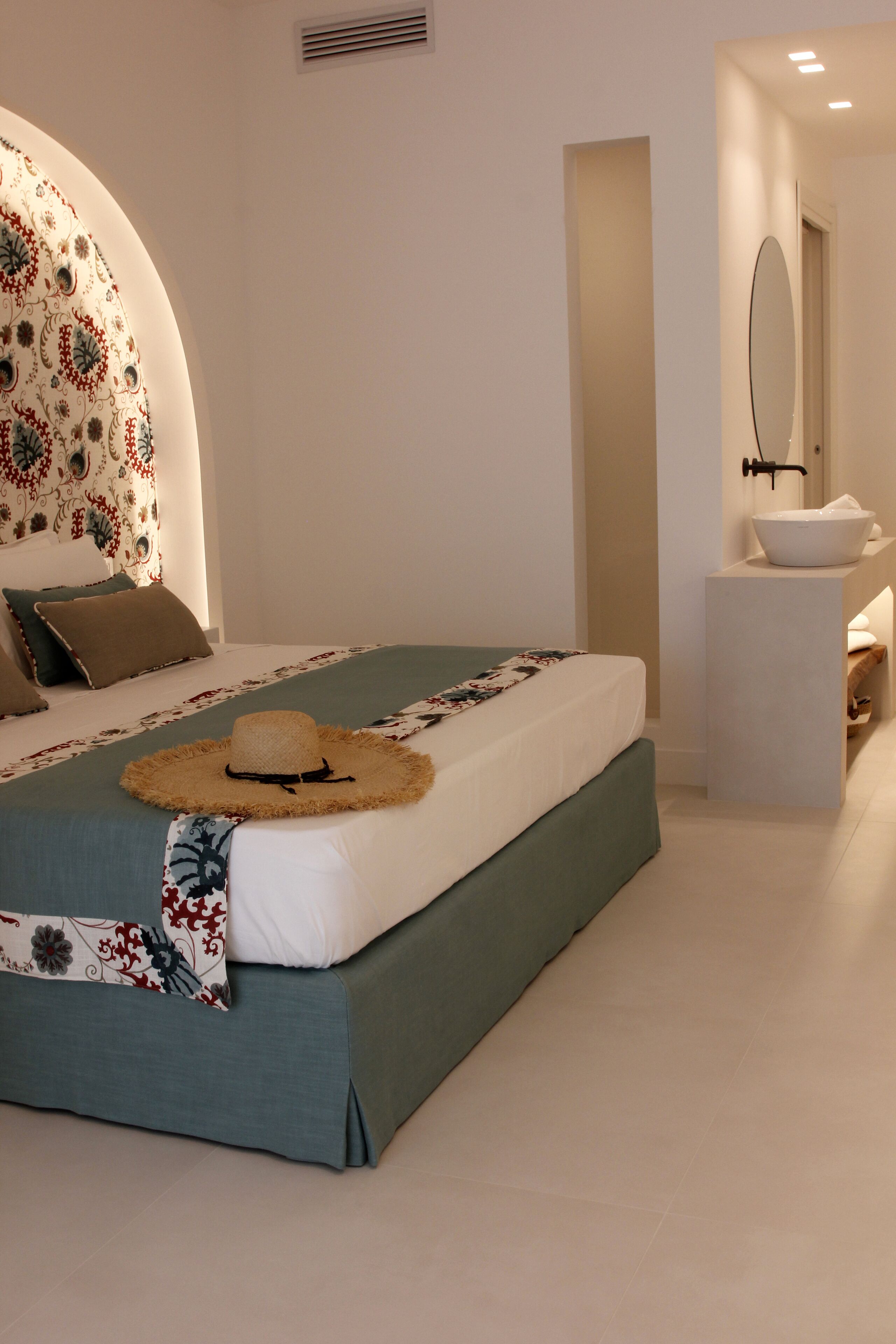 A modern bedroom with a large bed, a bedside table, a mirror, and a bathroom area.