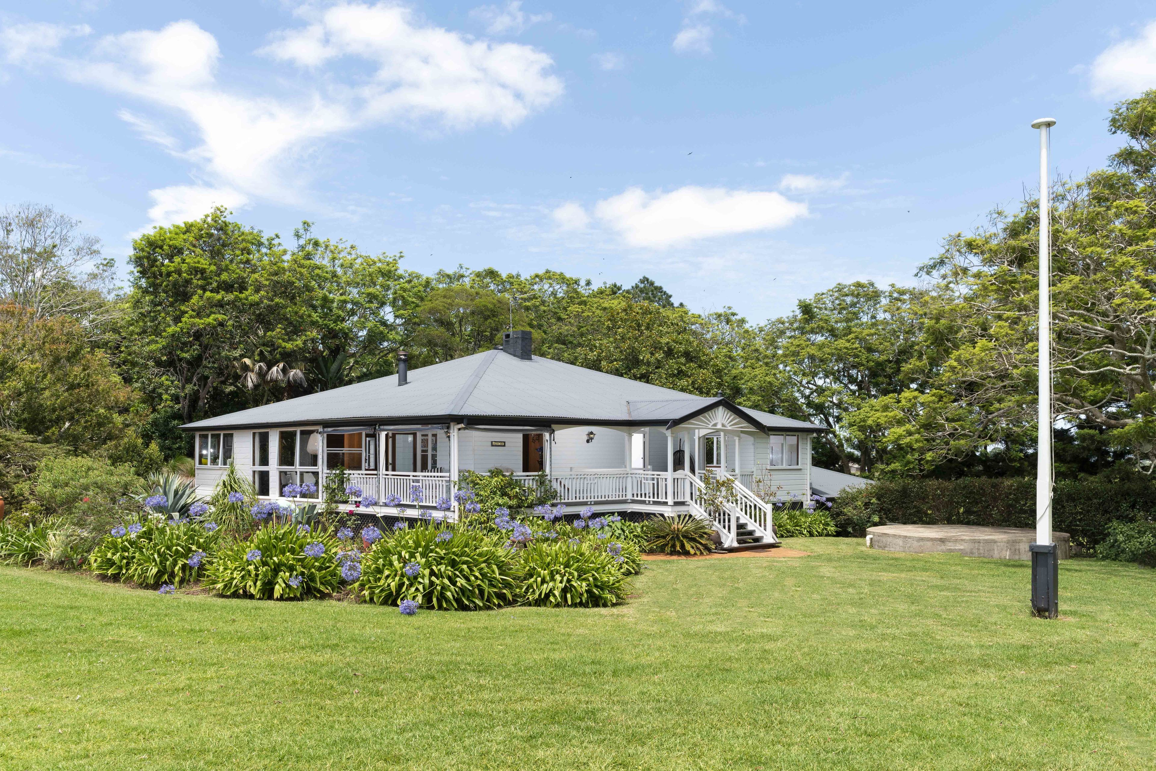 A two-story house with a porch, surrounded by a well-maintained lawn and flowering plants.