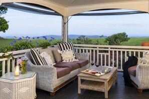 A covered outdoor seating area with wicker furniture, a glass table, and a view of a green landscape. - Rosewood Estate (Beechmont)