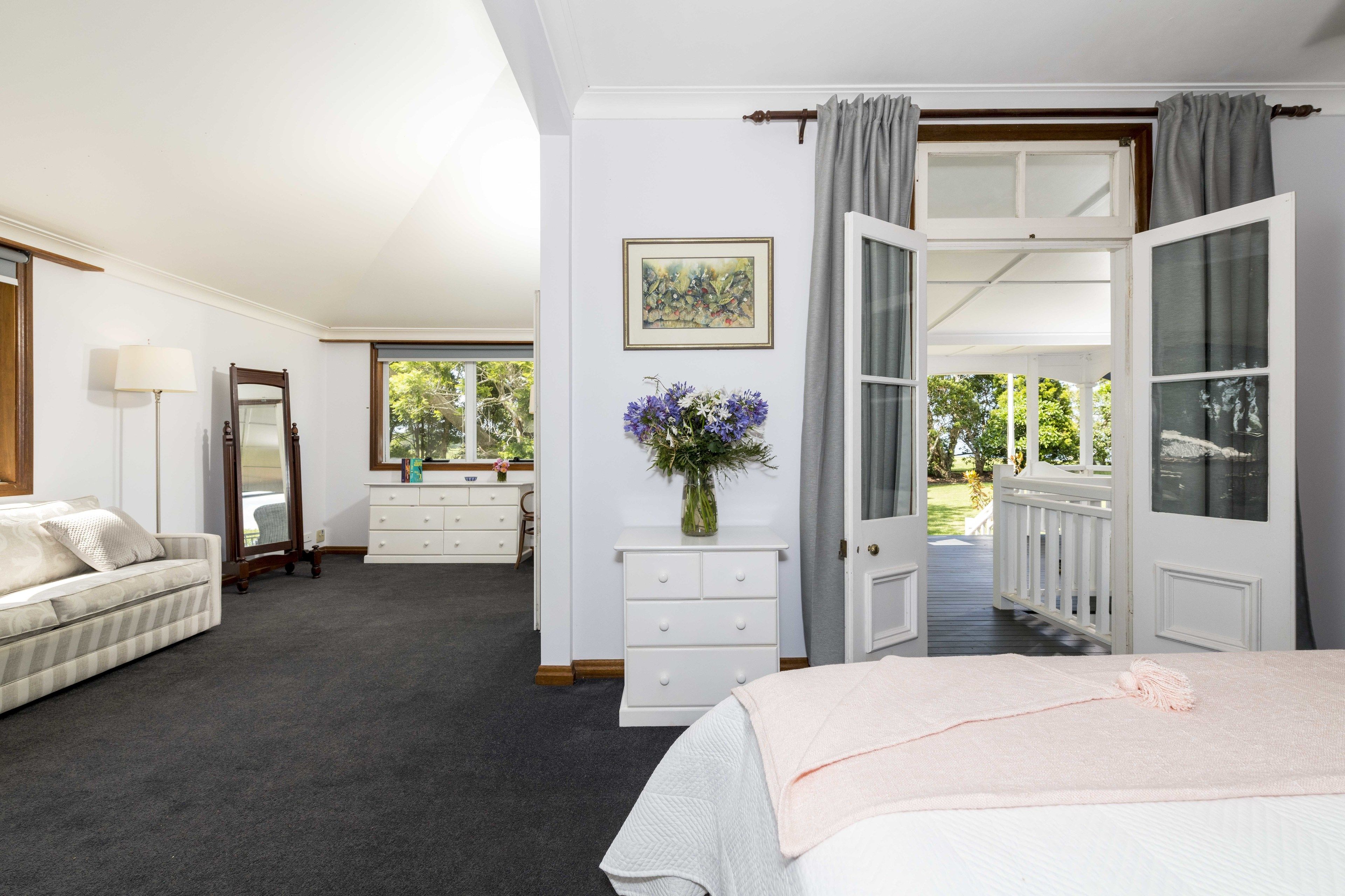 A bedroom with a bed, a dresser, a mirror, a vase with flowers, and a window with curtains.