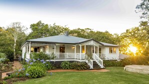 A two-story house with a covered porch, a front staircase, and a well-maintained garden with various plants and flowers. - Rosewood Estate (Beechmont)