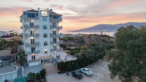 Un hôtel à plusieurs étages doté de balcons, d’un parking et offrant une vue sur la mer et les collines.