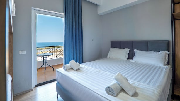 Une chambre avec un lit, un balcon avec une table et une vue sur la mer.