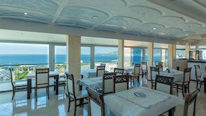 Un restaurant doté de tables et de chaises, de grandes fenêtres offrant une vue sur la mer et d’un plafond au design unique.