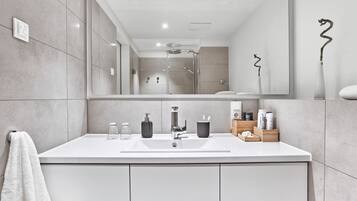 A modern bathroom with a large mirror, a shower, and a white sink with toiletries.