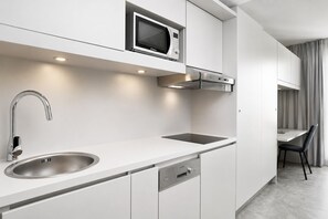 A modern kitchen with a built-in microwave, stainless steel sink, and a compact stove. - BD Munich Olympiapark (Munich)
