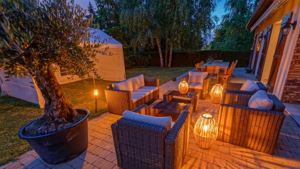 An outdoor patio with wicker furniture, a large potted tree, and ambient lighting. - Le Clos Magedon (Médan)