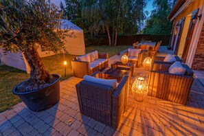 An outdoor patio with wicker furniture, a large potted tree, and ambient lighting. - Le Clos Magedon (Médan)