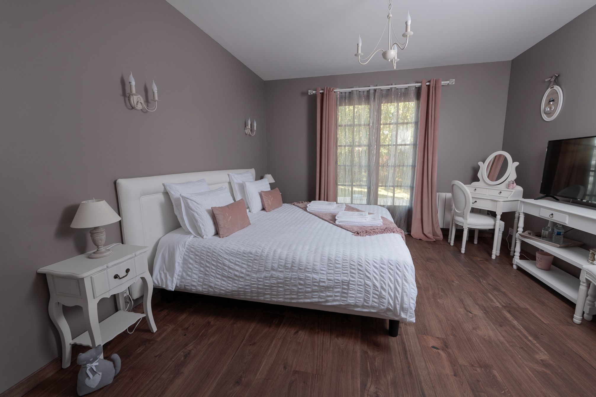Un dormitorio con cama, mesita de noche, lámpara, cómoda, espejo y televisor.