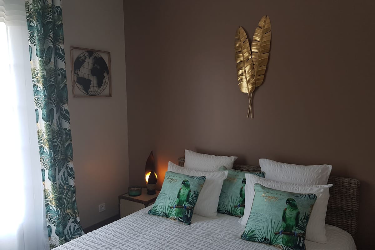 Un lit bien fait, avec une literie blanche et des coussins à motifs verts, une décoration murale représentant un globe terrestre et une feuille dorée décorative au plafond.