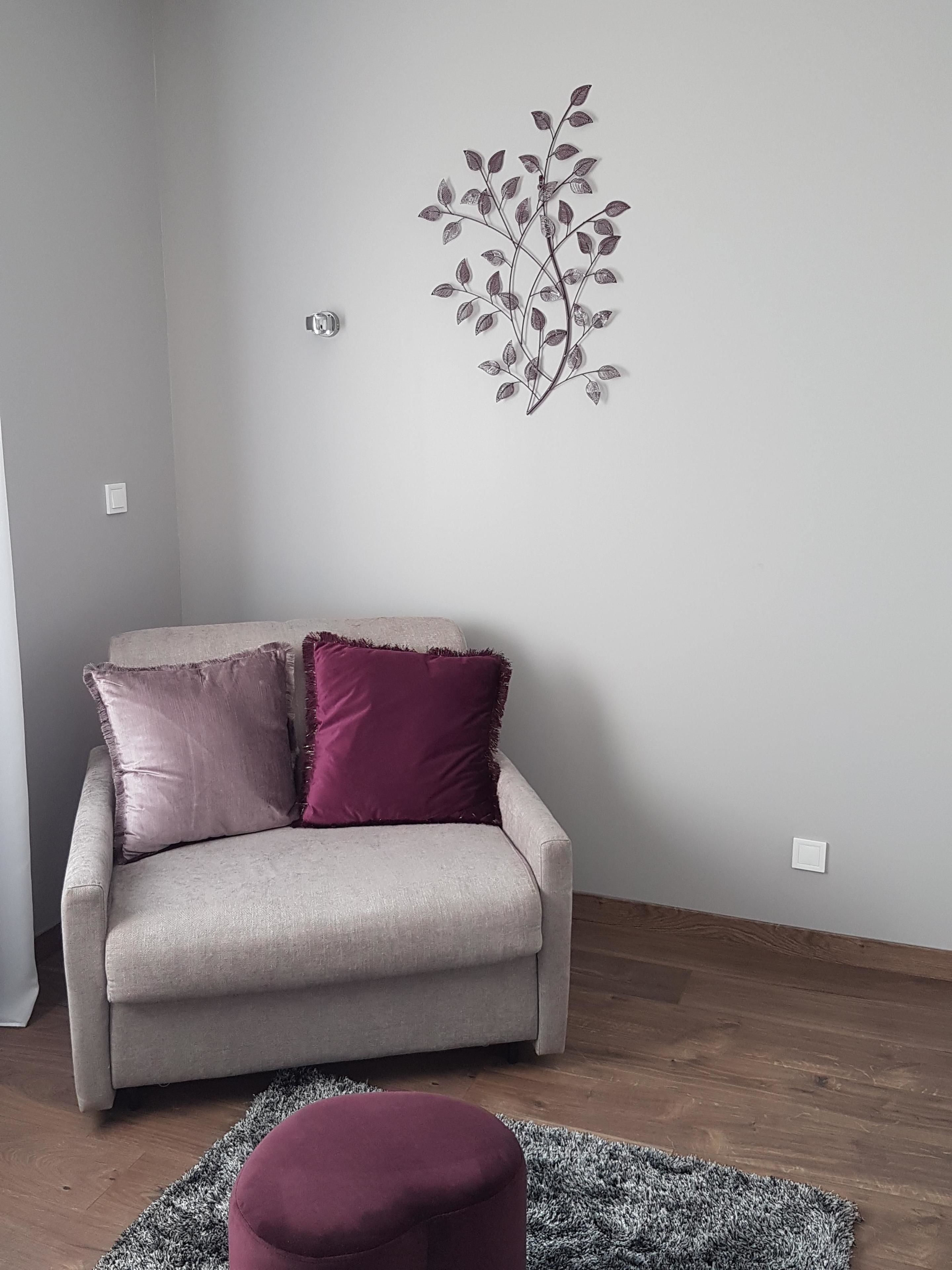 Una sala de estar con un sofá color beige, dos cojines, un adorno de pared y una alfombra gris.