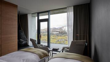 Habitación de hotel moderna con dos camas, un sillón colgante y vistas a un paisaje montañoso.