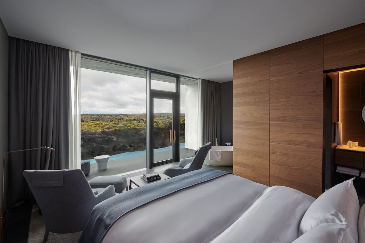 A modern hotel room with a large bed, a seating area with a view, and a wooden panel wall.