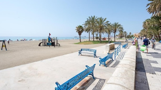 Une promenade en bord de mer, agrémentée de bancs bleus, de palmiers et offrant une vue dégagée sur la plage.