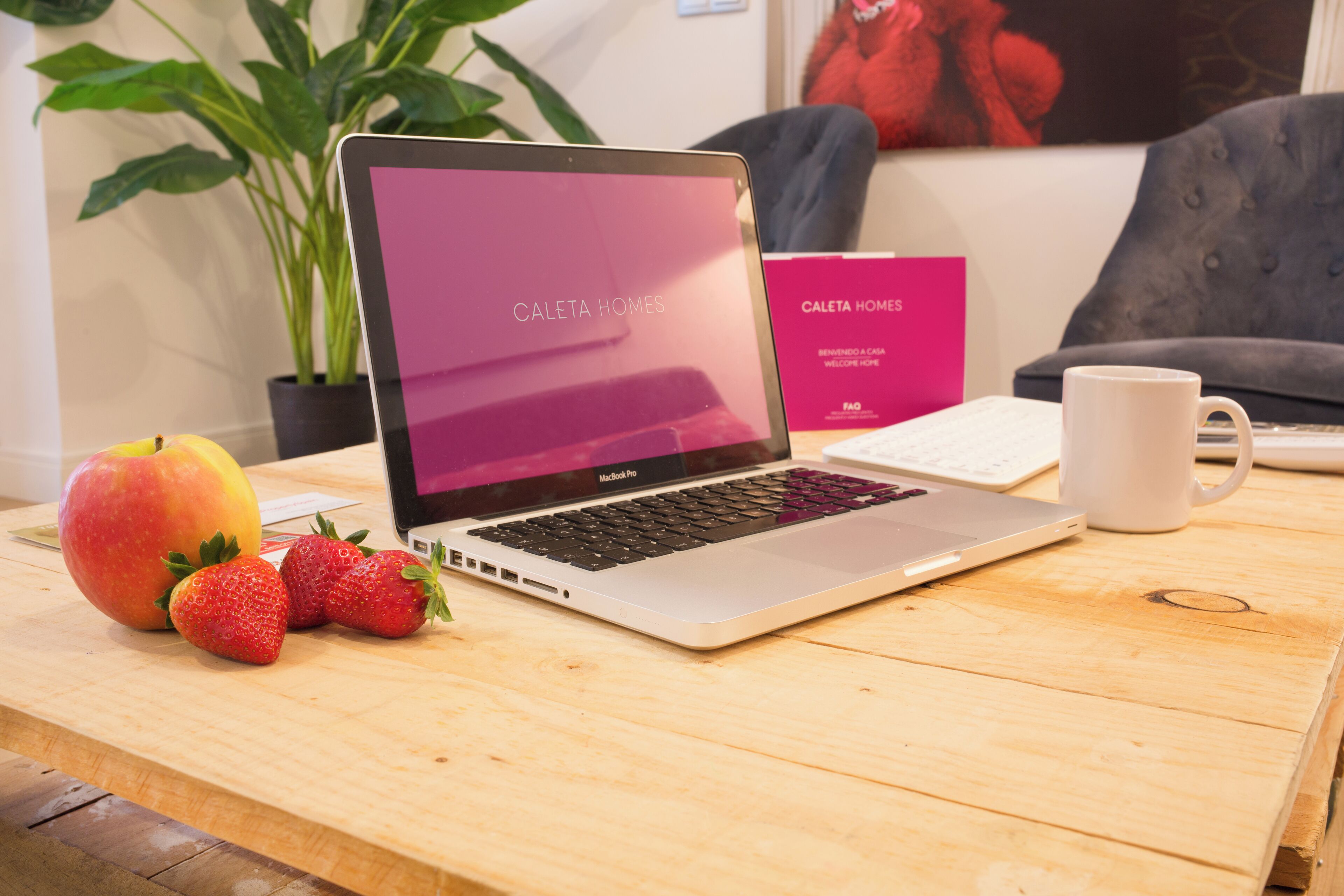 A laptop on a wooden table with a sign reading "Caleta Homes" and a plant in the background.