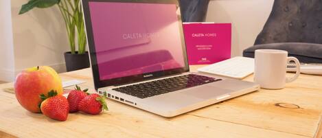 A laptop on a wooden table with a sign reading "Caleta Homes" and a plant in the background.