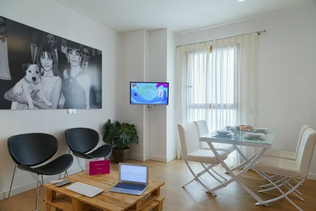 A modern living room with a dining area, a television, and a laptop on a wooden table.
