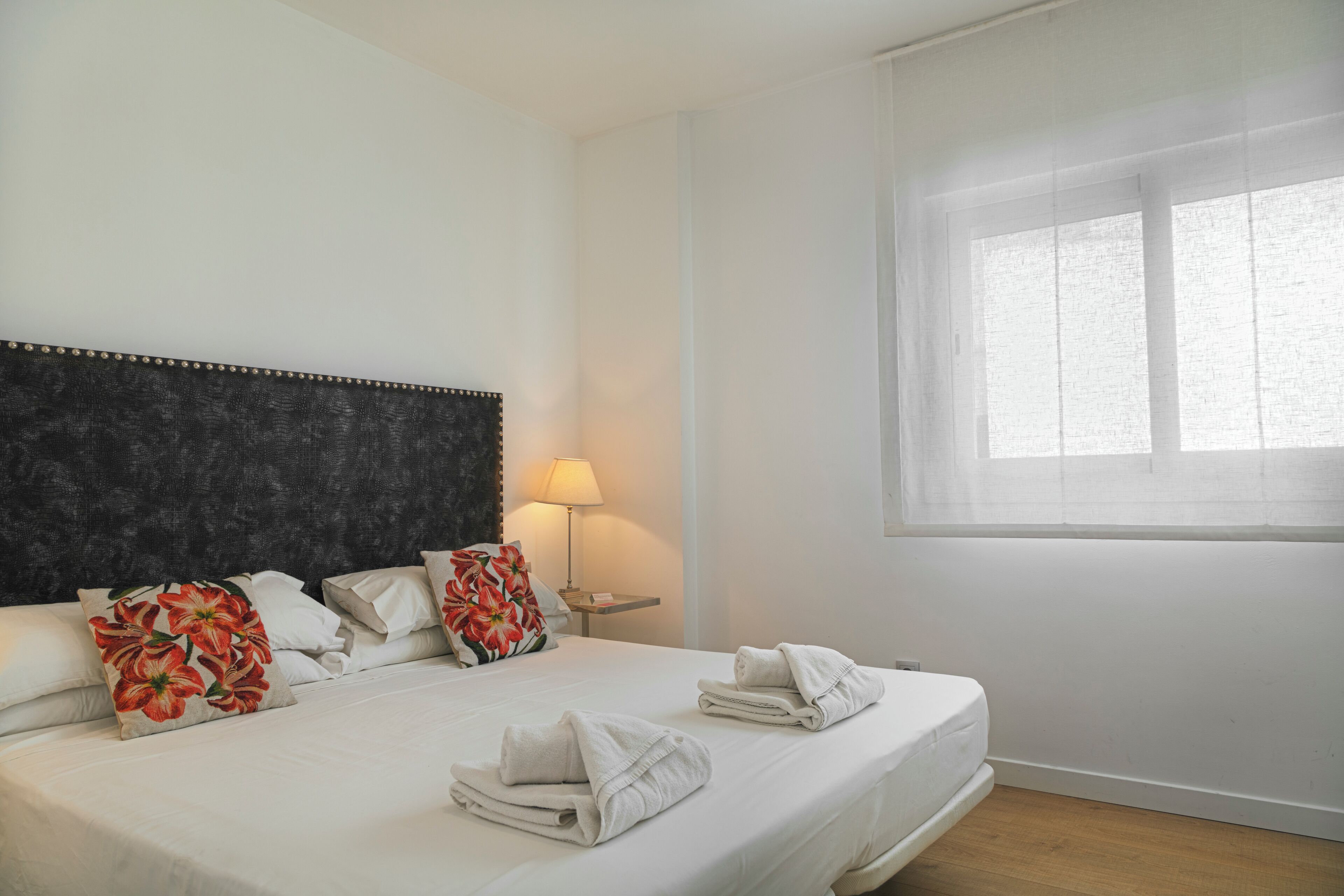 A hotel room with a bed, pillows, a lamp, and a window.