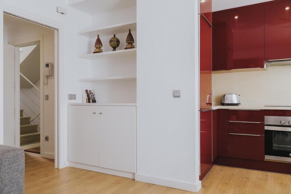 Une cuisine moderne avec des meubles rouges, un four encastré et un plan de travail sur lequel se trouve une bouilloire.
