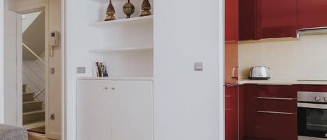 Une cuisine moderne avec des meubles rouges, un four encastré et un plan de travail sur lequel se trouve une bouilloire.