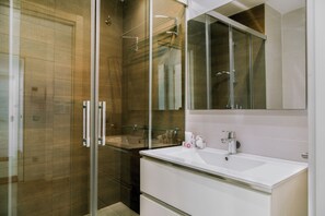 Ein modernes Badezimmer mit einer Duschkabine aus Glas, einem weißen Waschbecken und einem großen Spiegel über der Waschtischablage.