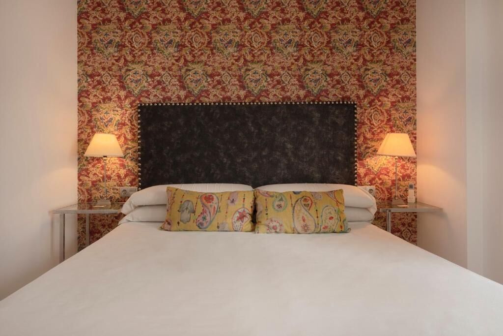 A bed with a dark headboard, two bedside lamps, and patterned pillows.