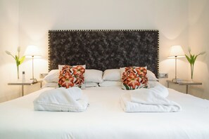 Ein Hotelzimmer mit einem großen Bett, zwei blumengemusterten Kissen, zwei Nachttischen mit Lampen und einem dunklen, strukturierten Kopfteil.