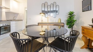 Une cuisine moderne avec des meubles blancs, une table de salle à manger ronde entourée de chaises noires, un miroir décoratif et une plante en pot.