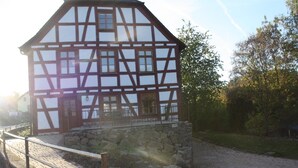 A half-timbered building with a stone foundation, a paved pathway, and a wooden fence. - Landhaus Hui Wäller (Greifenstein)