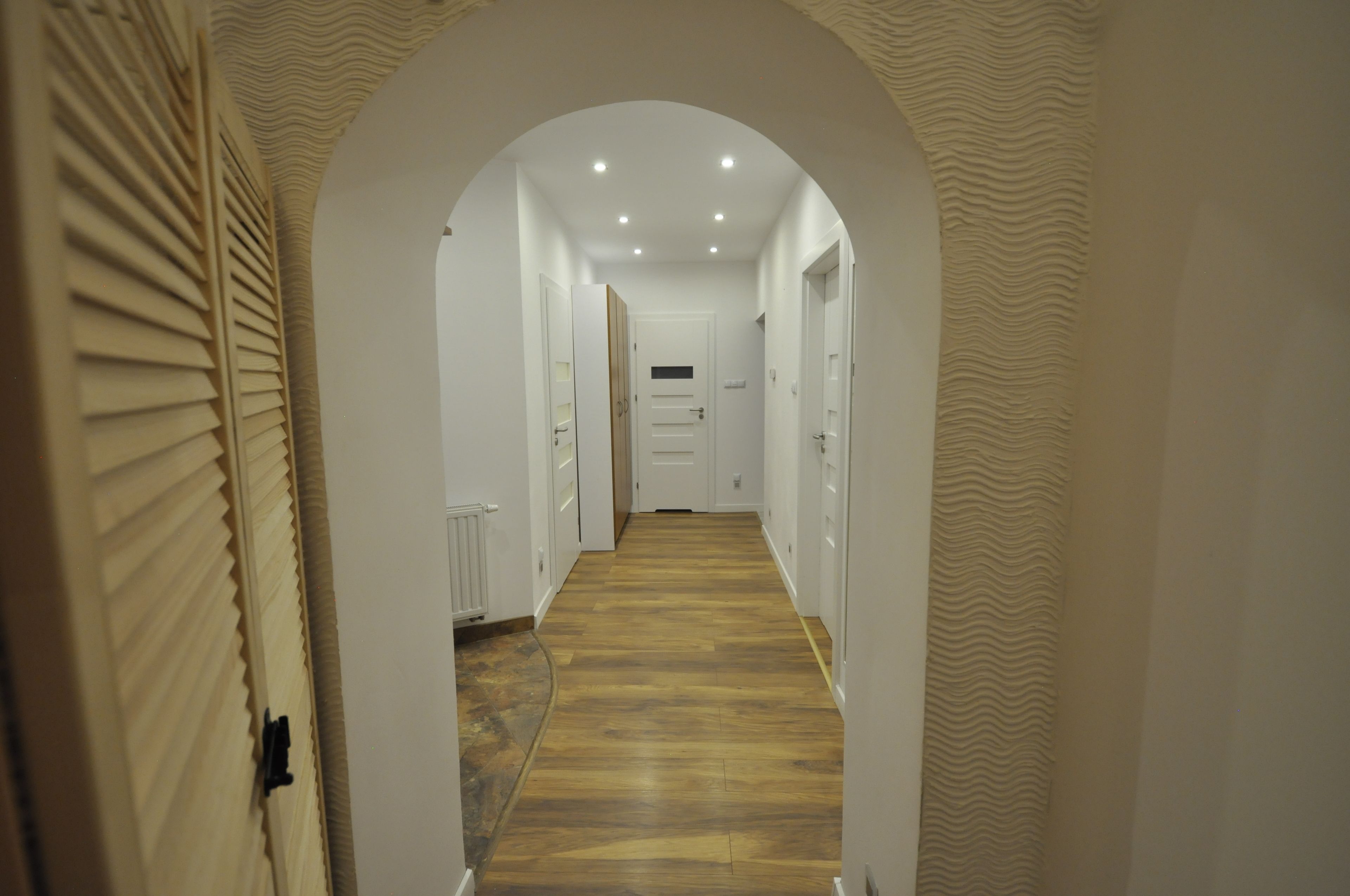 A hallway with a wooden floor, white walls, and an arched ceiling.