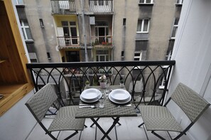 A balcony with two wicker chairs and a table set for two, overlooking a building with balconies. - WS Sauna Apartments (Kraków)