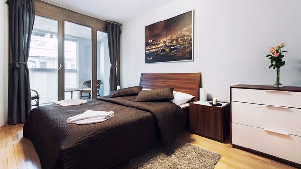 Ein modernes Schlafzimmer mit einem großen Bett, einem Nachttisch, einer Kommode und einem Stadtbild an der Wand.
