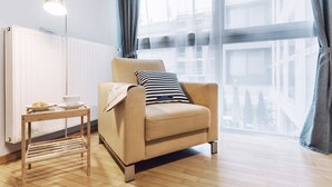 Ein modernes Wohnzimmer mit einem beigefarbenen Sessel, einem kleinen Holztisch mit Lampe und Blick auf eine Stadtlandschaft durch große Fenster.