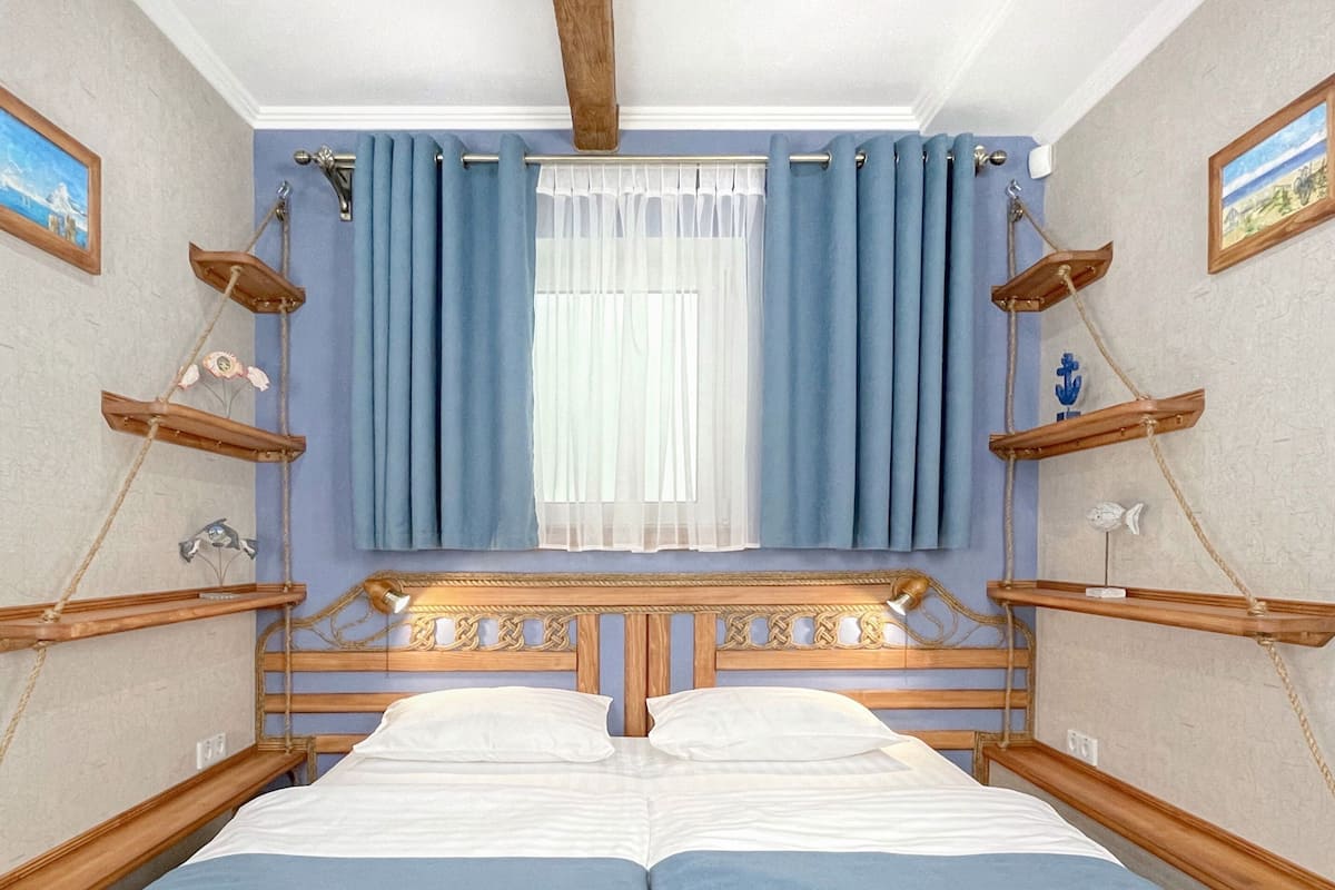 A double bed with a wooden headboard, blue curtains, and a view of the room's interior.