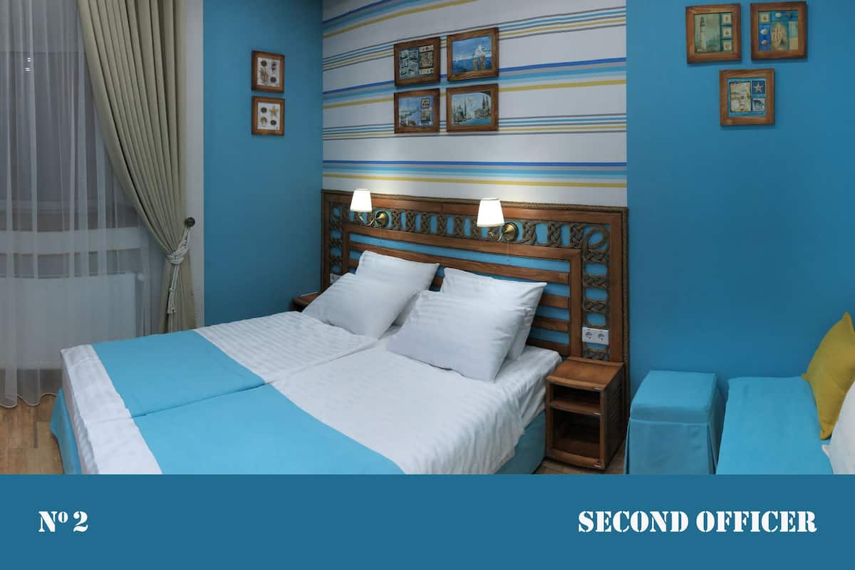 A hotel room with a large bed, two bedside tables, a headboard with a decorative design, and a striped wall with framed pictures.