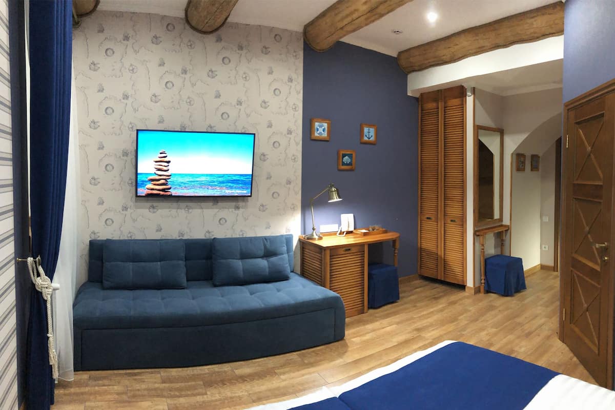 A cozy room with a curved blue sofa, a wooden desk with a lamp, and a TV on the wall.