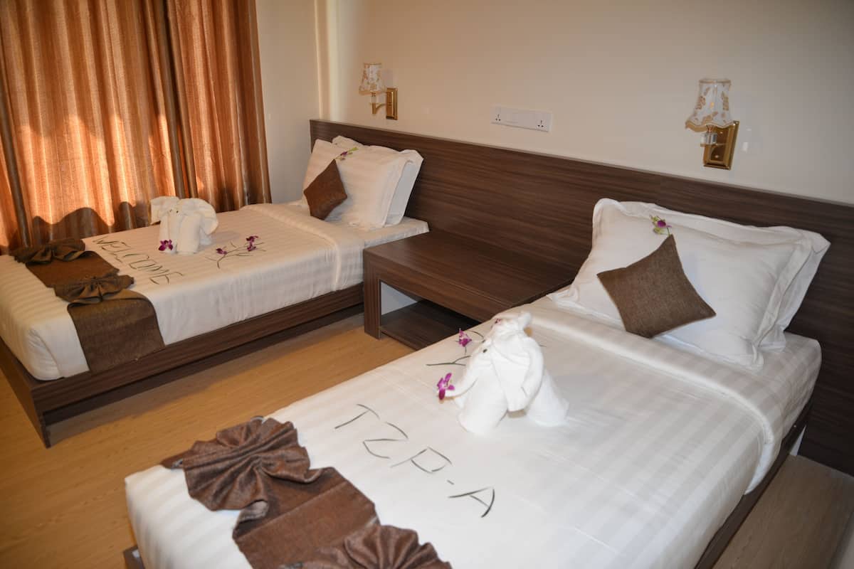 Two twin beds with towels and a welcome sign, a wooden bench, and a wall-mounted lamp.