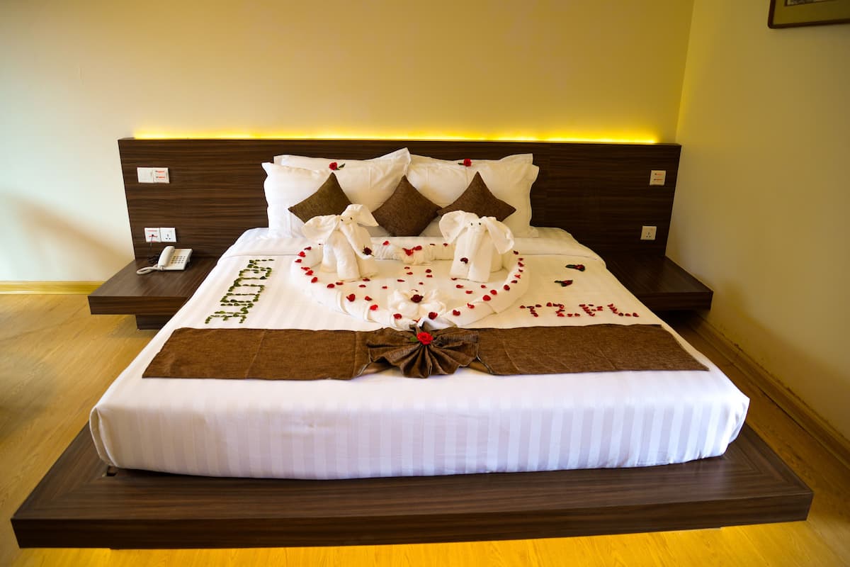A neatly made bed with a white and brown bedspread, a decorative bow, and rose petals.