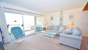 A living room with a sofa set, a blue chair, a coffee table, and a balcony with chairs and a table. - Beachmark 3F - 1 Bedroom Condo by RedAwning (Ocean City)