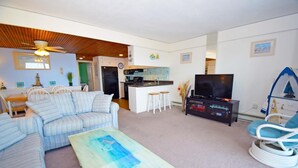 A living room with a sofa, a coffee table, a TV, and a kitchen area in the background. - Beachmark 3F - 1 Bedroom Condo by RedAwning (Ocean City)