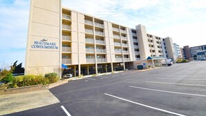 A beachfront condominium with multiple balconies, a parking lot, and a small outdoor seating area. - Beachmark 3F - 1 Bedroom Condo by RedAwning (Ocean City)