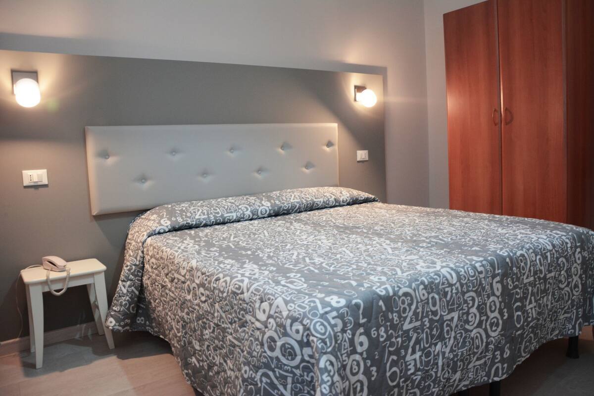A bedroom with a tufted headboard, a bed with patterned bedding, a bedside table with a phone, and a wooden wardrobe.