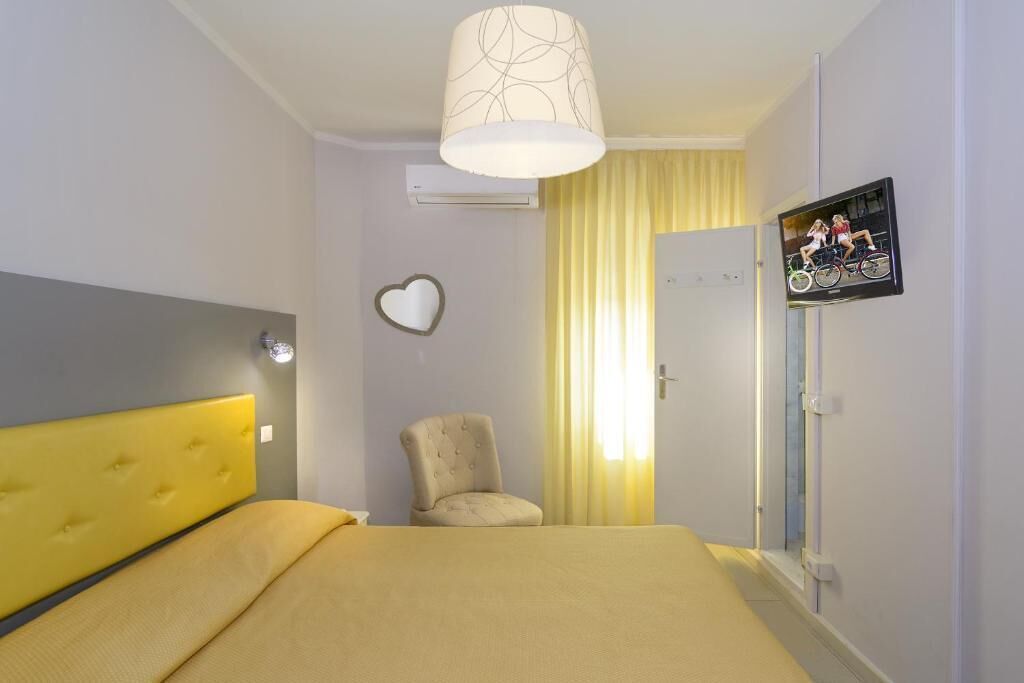 A hotel room with a bed, a chair, a heart-shaped decoration, and a television on the wall.