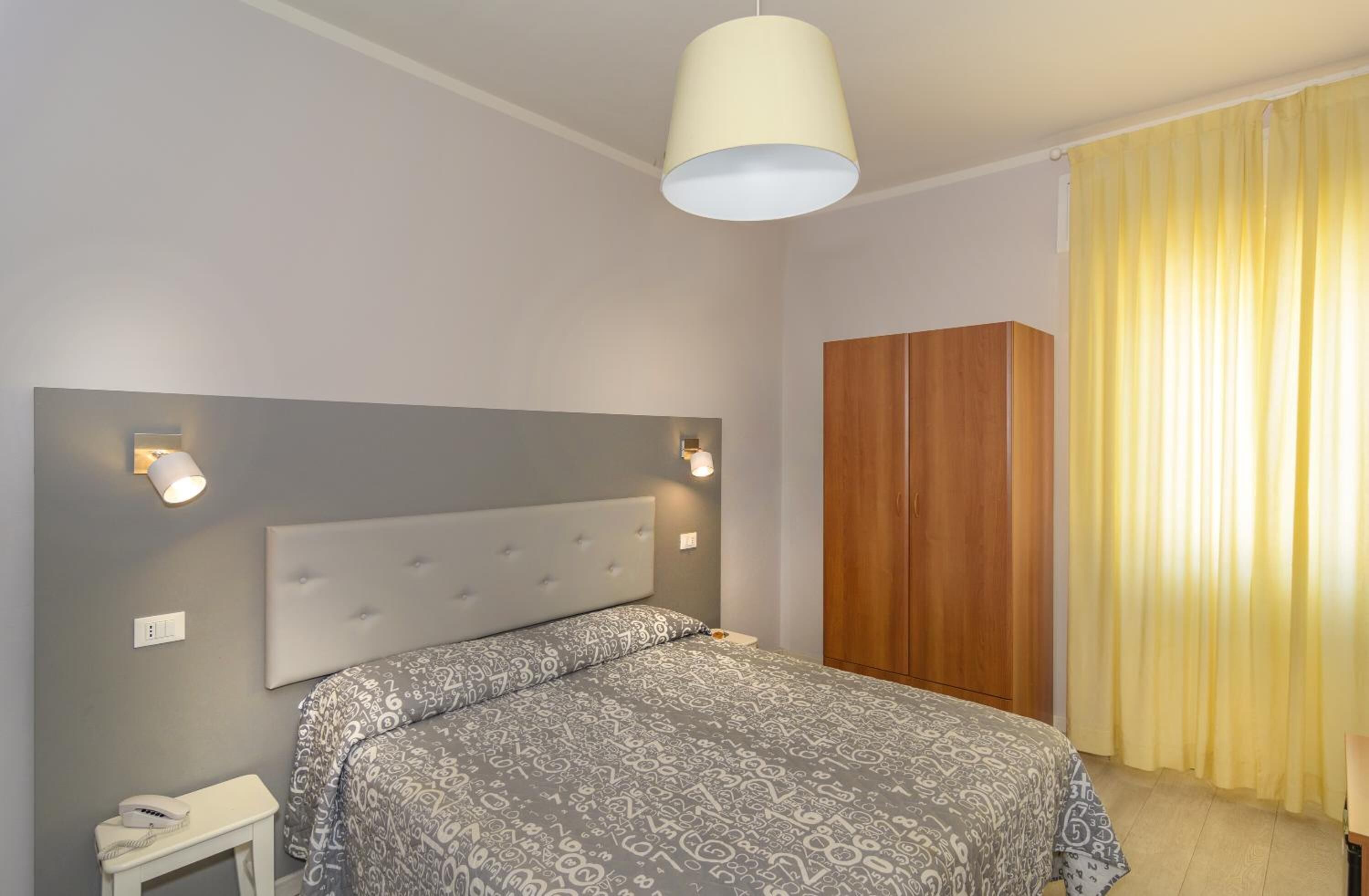 A bedroom with a large bed, a wooden wardrobe, a bedside table with a lamp, and a ceiling light fixture.