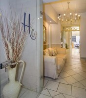 A hotel lobby with a reception desk, a chandelier, a sofa, and a vase with dried plants.