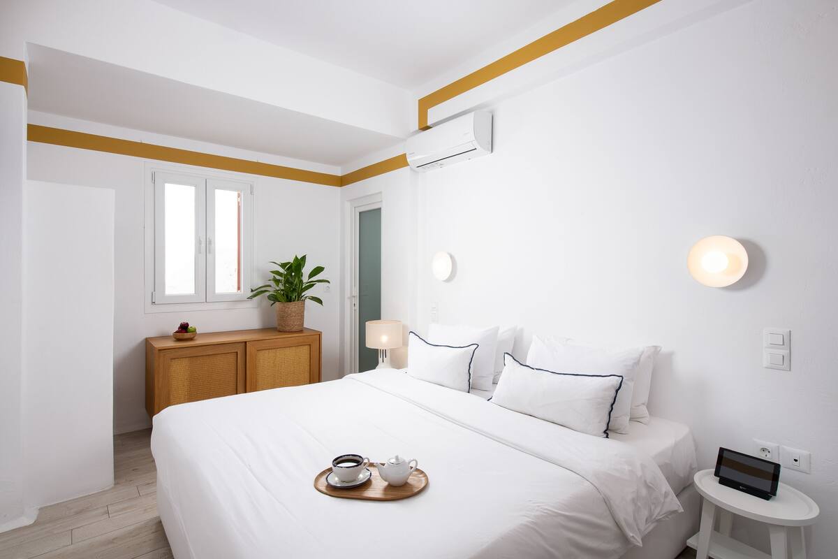 Una habitación de hotel con cama, mesita de noche, lámpara y una pequeña mesa con una bandeja de desayuno.