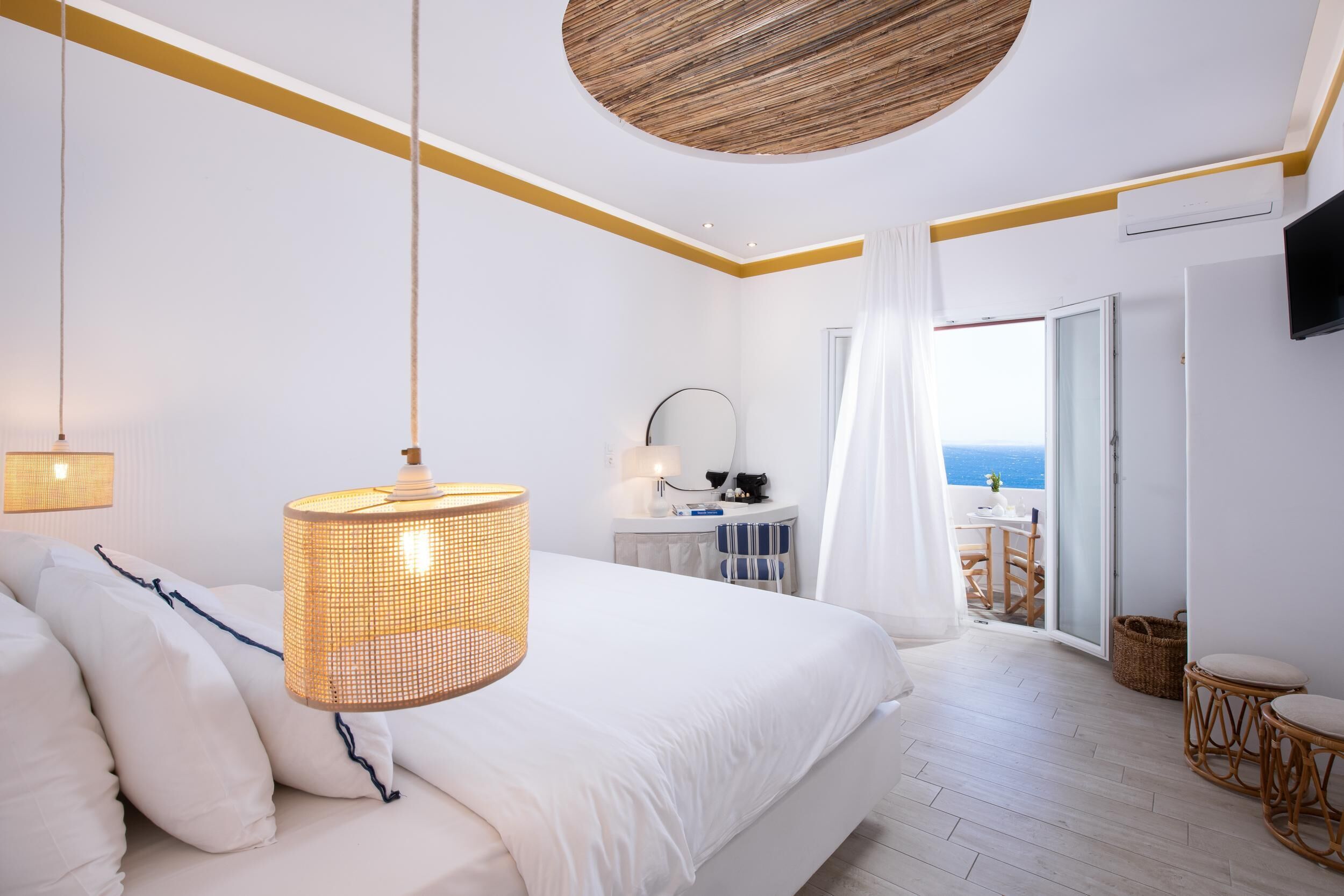 A bedroom with a bed, bedside lamp, and a view of the sea through an open door.