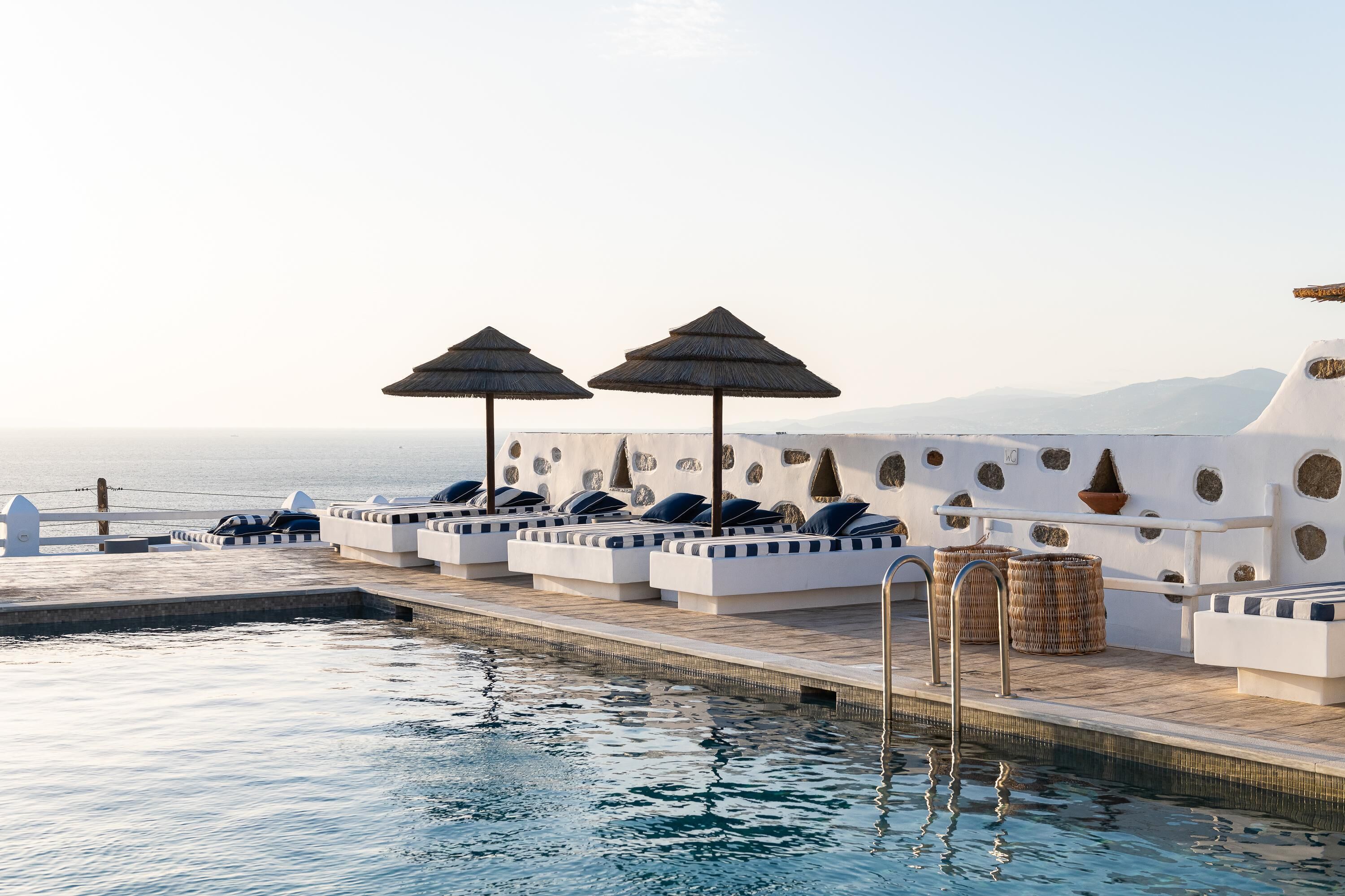 Zona de piscina con sillones de descanso y sombrillas, vista despejada al mar, y diseño arquitectónico moderno con ventanales circulares.